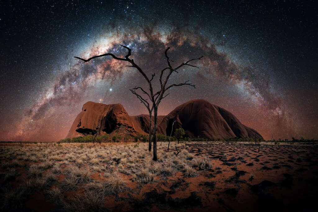 Uluru`s Night von Nacht- und Astrofotograf Stefan Liebermann - Night Panorama of the Uluru in Australia. In the foreground you can spot burned down trees and contrast between dry gras and burned down regions. In the sky is the milky way arch.